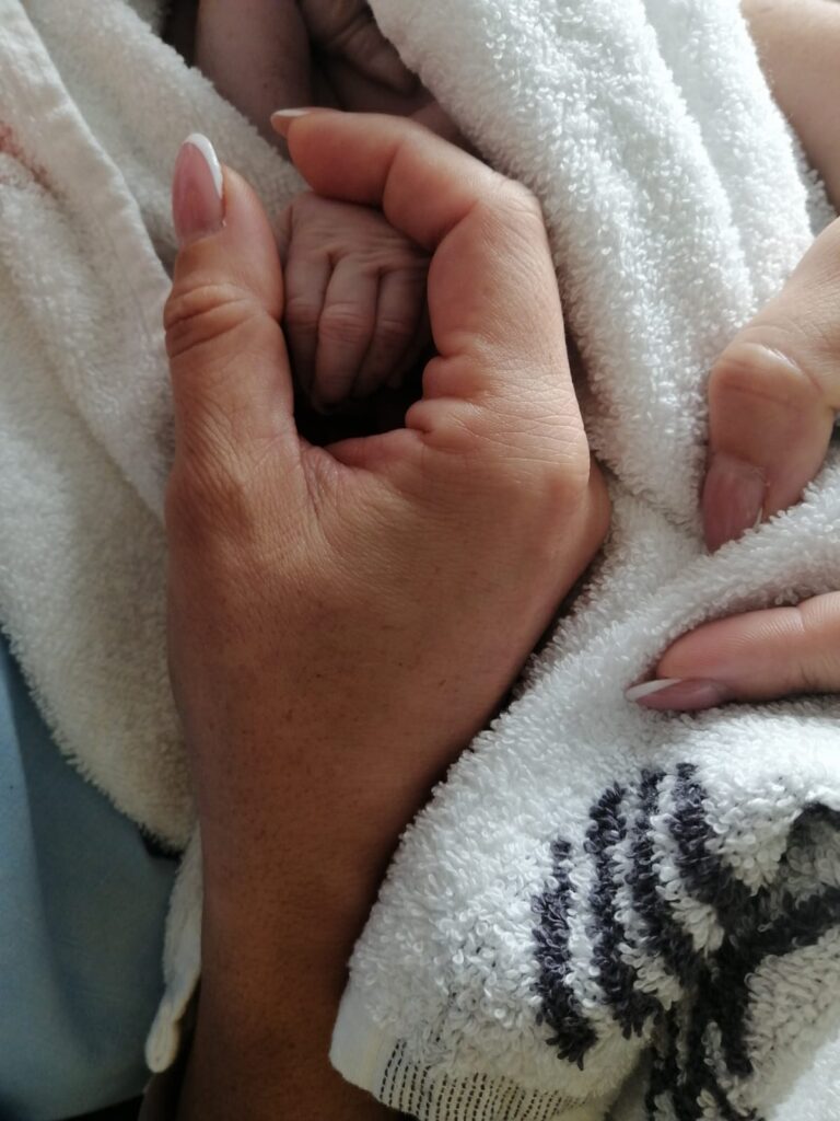 Manos sosteniendo a un bebé tras una pérdida durante el embarazo, imagen de duelo perinatal y acompañamiento emocional desde el amor