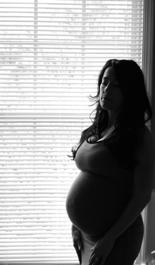 Mujer embarazada en contraluz junto a una ventana reflexionando sobre el duelo perinatal y el amor hacia su bebé